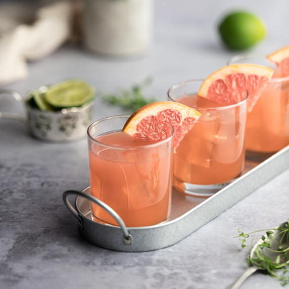 Three grapefruit crush cocktails, garnished with a slice of grapefruit, on a thin metal serving tray
