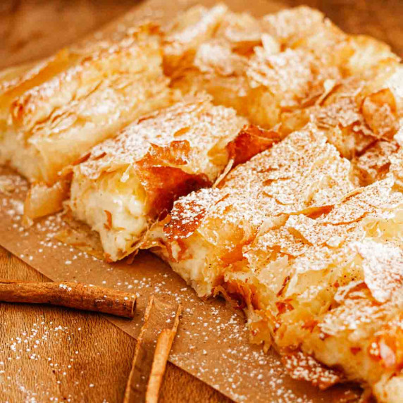 Greek bougatsa cut into squares on parchment paper and dusted with powdered sugar and cinnamon.