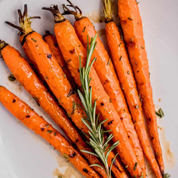 Whole grilled carrots arranged on a white plate with a fresh rosemary sprig garnish.