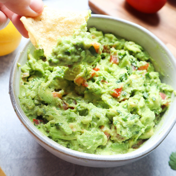 white bowl with guacamole without onion with a chip 