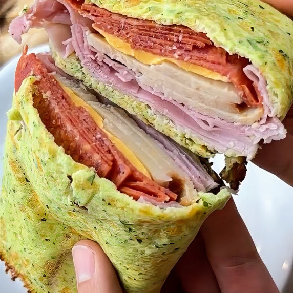 A hearty zucchini wrap held open to reveal layers of deli meats and melted cheese.