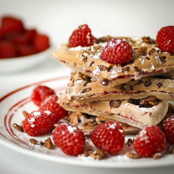 Close up shot of chocolate crunch raspberry waffles stacked on a white plate.