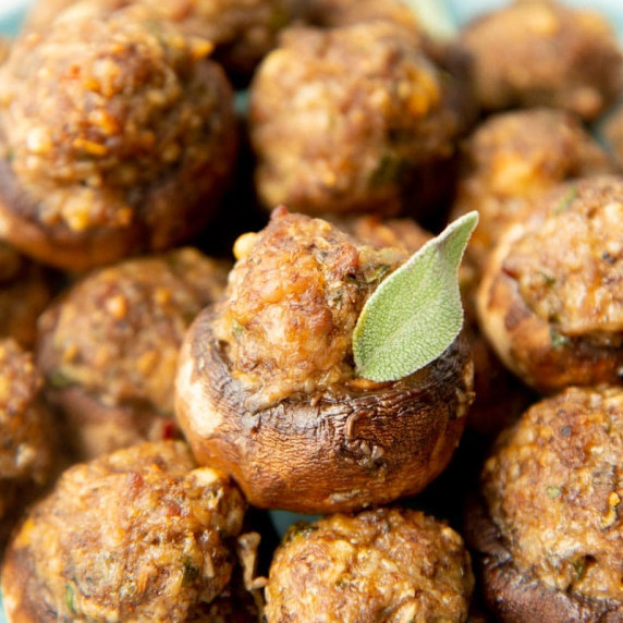 A parmesan and sausage stuffed mushroom cap with a sage leaf garnish sits atop other stuffed caps.
