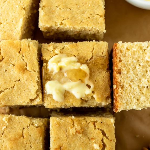 squares of cornbread on parchment paper topped with a pat of butter.