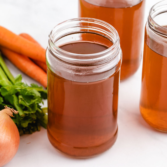 Vegetable broth in jars with carrots, celery, and onion.