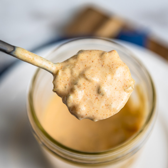 Close up shot of a spoon holding up a spoonful of big mac sauce over a mason jar full of sauce.