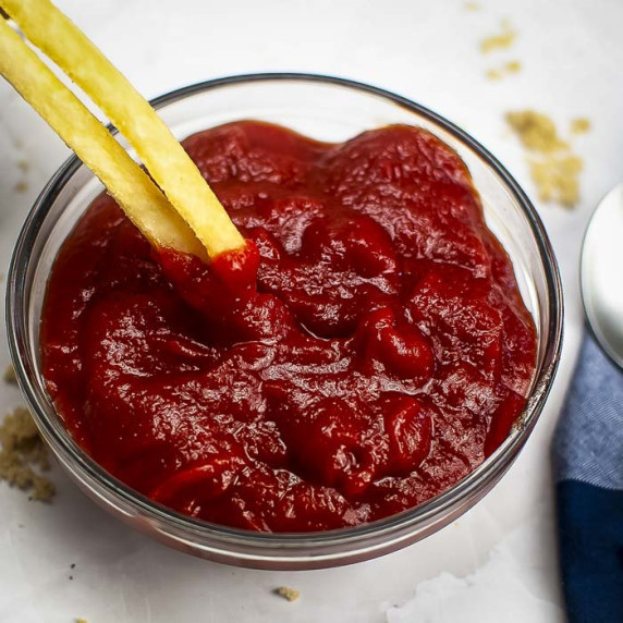 Close up shot of two french fries being dipped into homemade ketchup in a clear bowl.