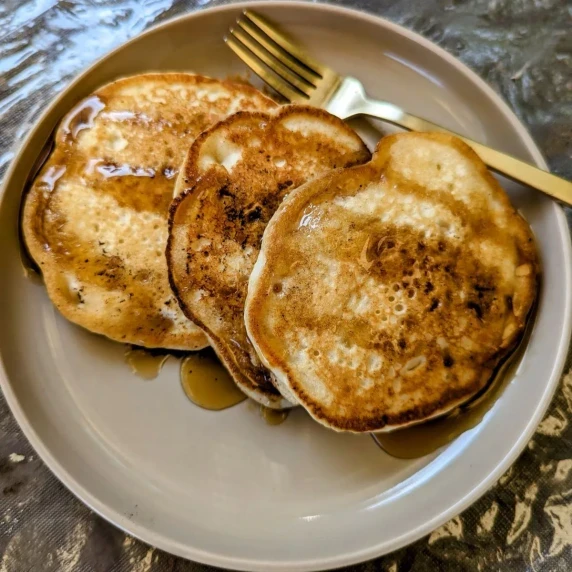 Three griddle cakes on a plate with syrup. 