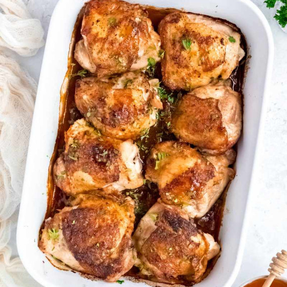 Overhead of eight honey garlic chicken thighs nestled in a white baking dish with a sticky sauce.