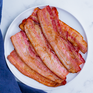 How to Cook Bacon RECIPE with an overhead angle of several strips of cooked bacon on a white plate.