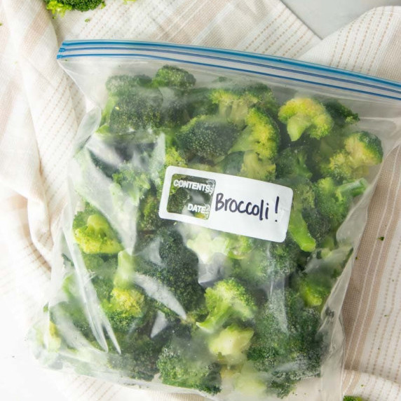A zip-lock freezer bag filled with frozen broccoli florets rests on a kitchen linen.