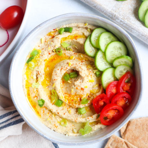 white bowl with lemon dill hummus topped with cucumber and tomatoes