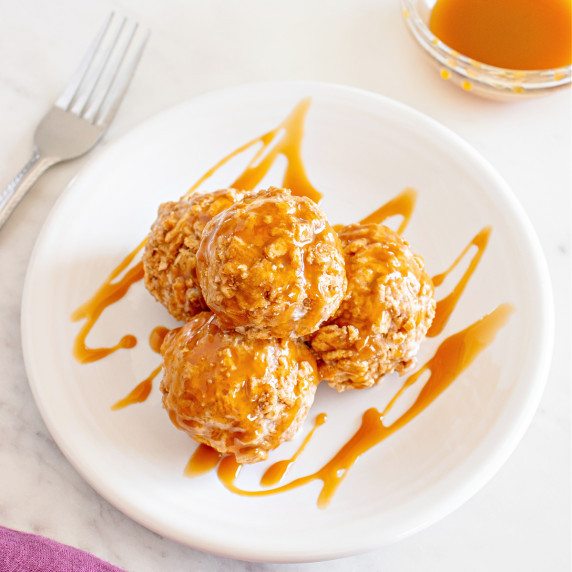 Plate of ice cream balls coated in cereal and drizzled with caramel sauce.