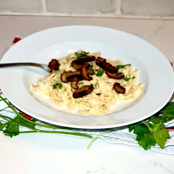 vegan pasta carbonara with mushrooms on a white plate over parsley