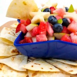 Fruit salsa in a star-shaped bowl with a chip dipping into it, more chips scattered around the bowl.