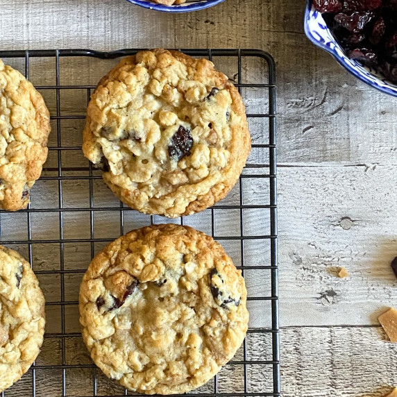 Cherry and toffee oatmeal cookies on a cooling rack on a wooden surface.