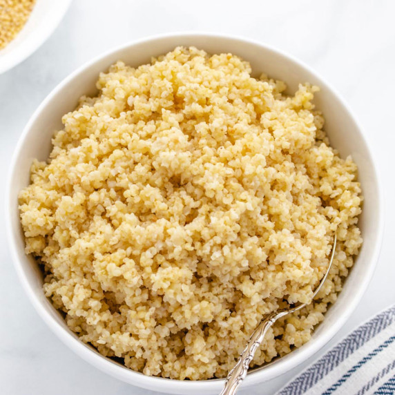 Cooked millet in a white bowl with a spoon.