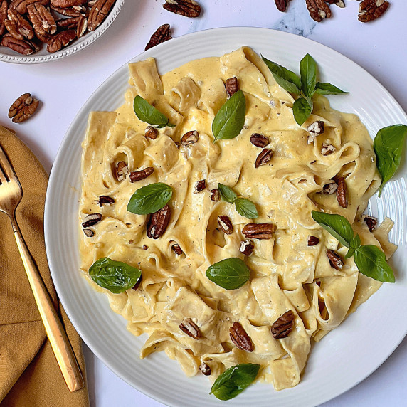 instant pot pumpkin pasta topped with pecans and basil on a white plate
