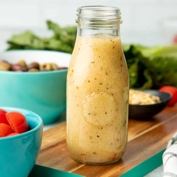 Close view of a glass jar filled with homemade italian salad dressing with fresh ingredients around.