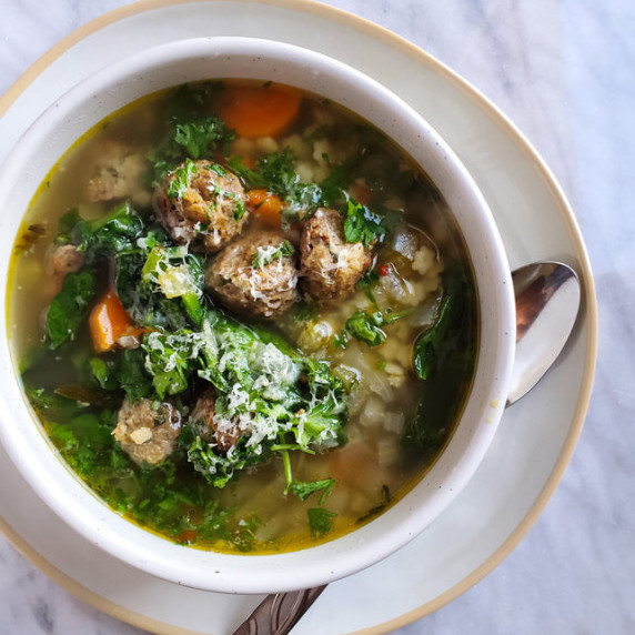A comforting bowl of meatballs, tender kale, grated hard cheese, and noodles.