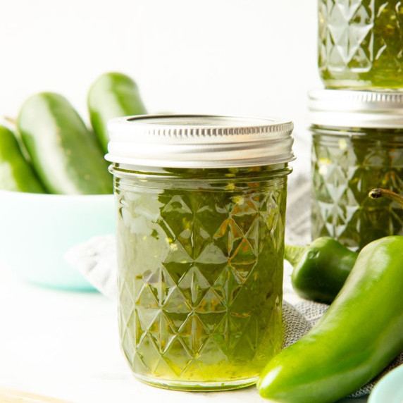 Close view of a half-pint jar of jalapeno jelly with fresh green jalapenos and addition jars around.