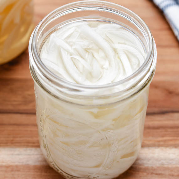 Slices of pickled white onions in a glass jar.