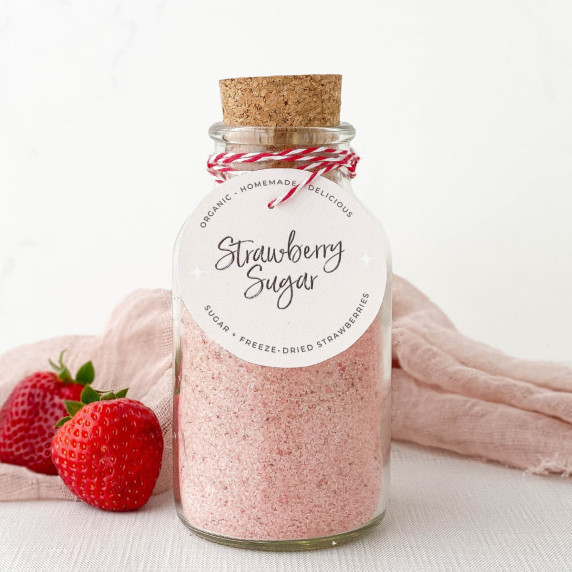 Glass jar of Strawberry Sugar with fresh strawberries nearby.
