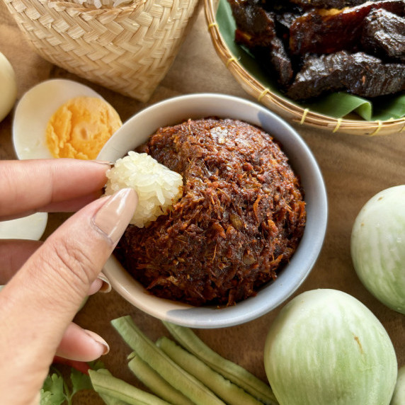 Hand dipping sticky rice into jeow bong, a Lao spicy chili paste, accompanied by veggies.