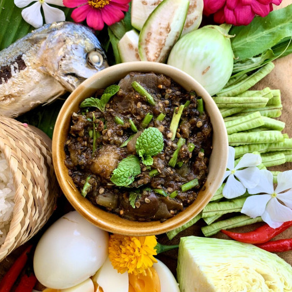 Top-view of jeow mak meua, a Lao eggplant dipping sauce, surrounded with fresh vegetables and more.
