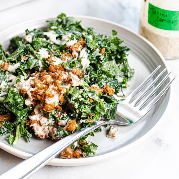 kale tahini Caesar salad on a plate with a fork.