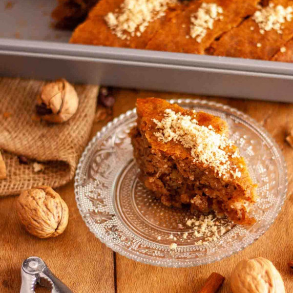 A slice of Greek walnut cake, karidopita, on a glass plate on a wooden surface next to walnuts.