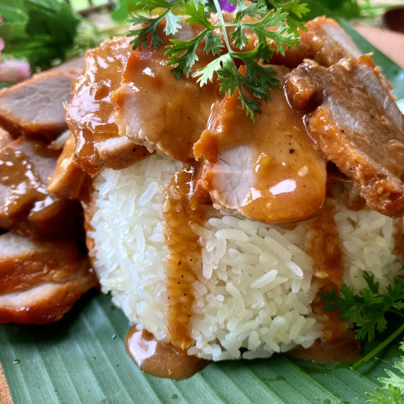 Khao moo dang (Thai red pork) served over jasmine rice, drizzled with red sauce.