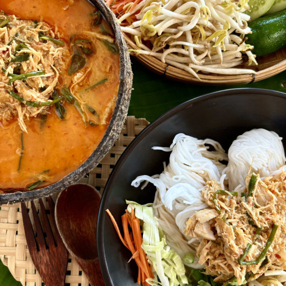 Top-view of khao poon, a red curry coconut milk broth, and fresh vegetables.