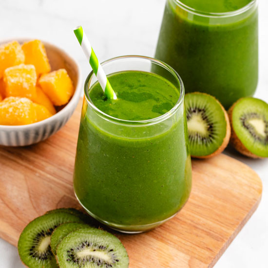 A kiwi mango smoothie in a glass with a straw and sliced kiwis.