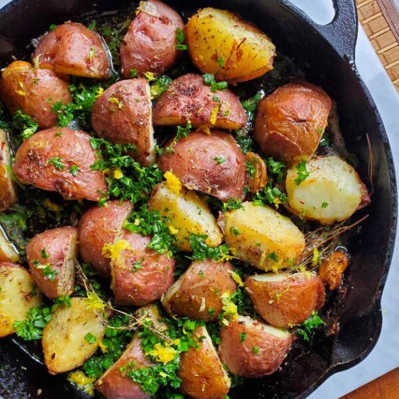 A black skillet filled with roasted red potatoes, bright yellow zest, and green herbs.