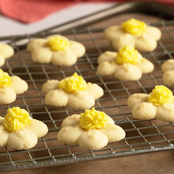 Flower shaped cookies with yellow icing for the middle, sitting on a wire rack.