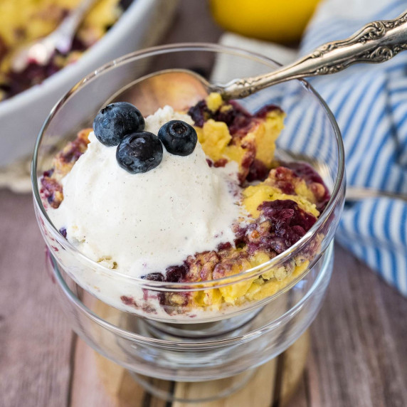 A serving of lemon blueberry dump cake in a glass dish topped with a scoop of vanilla ice cream. 