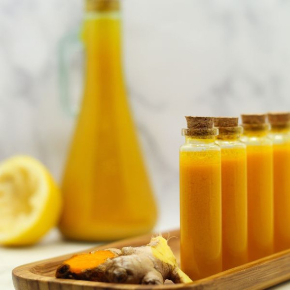 Orange colored Lemon Ginger Turmeric Wellness Juice Shots in tiny glass vials on a wooden plate.