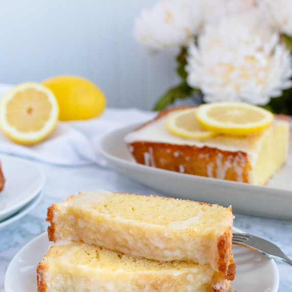 Two slices of lemon loaf on a plate with lemons in the background