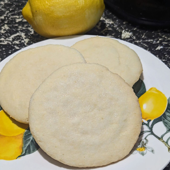 Three lemon sugar cookies on a plate with a lemon in the background.