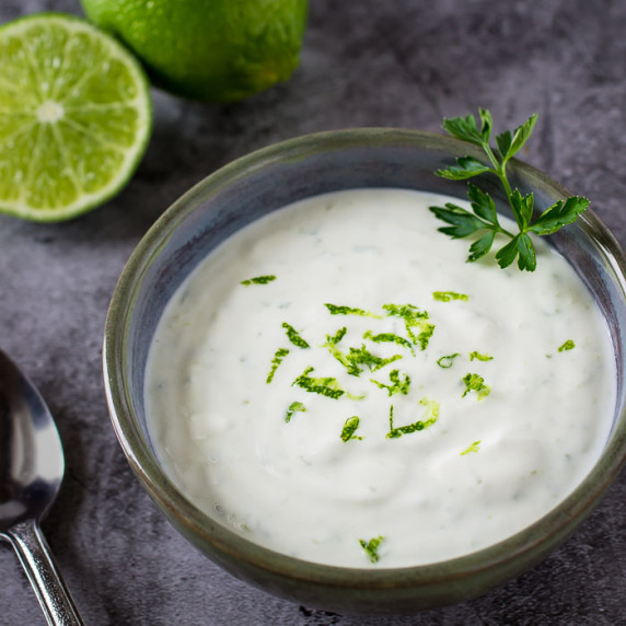Overhead shot of lime cream garnished with herbs and lime zest in a clear bowl.