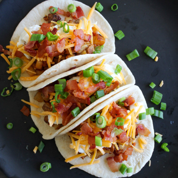 Three loaded baked potato tacos on a plate garnished with scallions