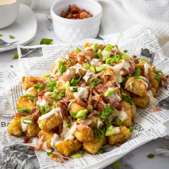 Side shot of loaded tater tots on a plate with newspaper parchment paper.