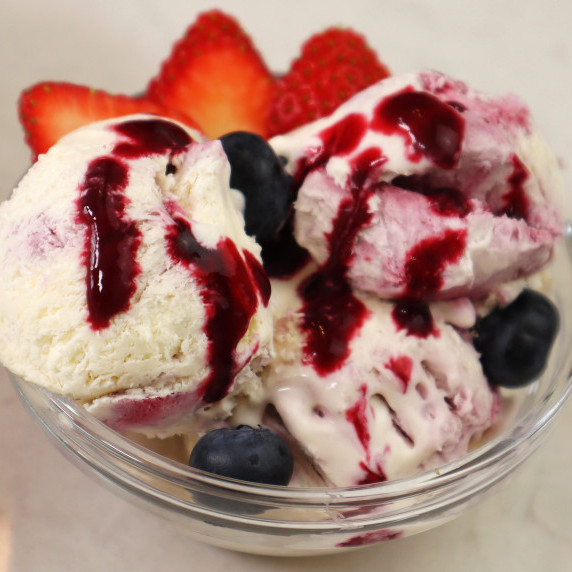 White and pink ice cream in a glass bowl decorated with blueberries, strawberries and red sauce.