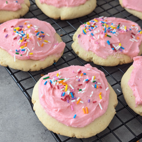 Lofthouse style cookies with pink frosting and sprinkles on a wire rack.