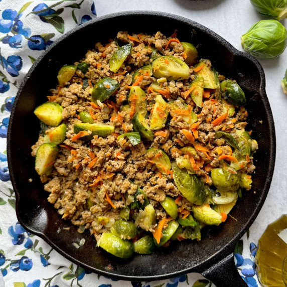 Ground turkey and brussel sprouts in the skillet next to olive oil bottle, sprouts and spices.