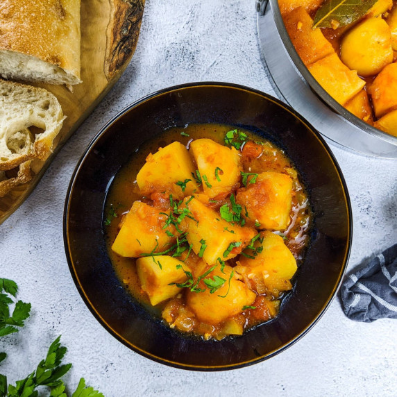 Greek tomato potatoes stew served in black bowl with chopped parsley on top and slices of bread next