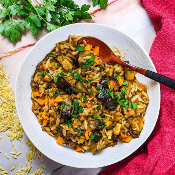 Mediterranean lentil, orzo and roasted eggplant stew served on white dish next to orzo and parsley.