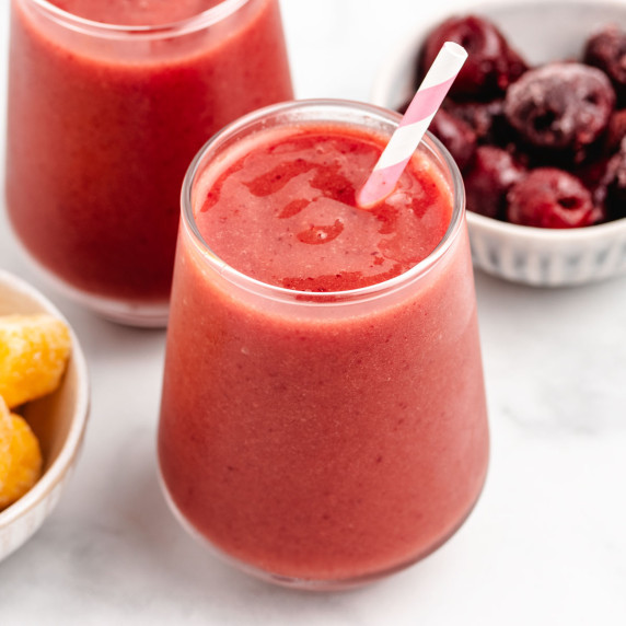 Cherry mango smoothie in a glass with a striped straw.