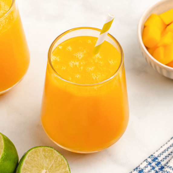 Mango water in a glass with a straw and limes and diced mango in the background.